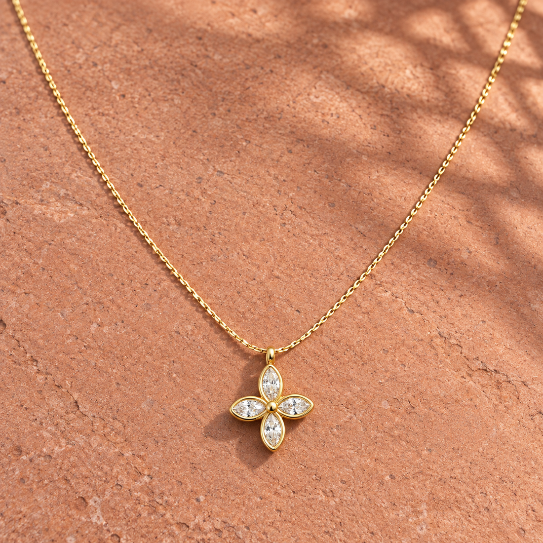 Gold-tone 316L stainless steel necklace with a cable chain and a four-petal flower pendant set with clear marquise stones, lying on a stone surface