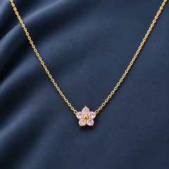 Gold-tone 316L stainless steel necklace with a fine cable chain and a flower pendant set with pink stones and a gold-tone centre, on a navy fabric