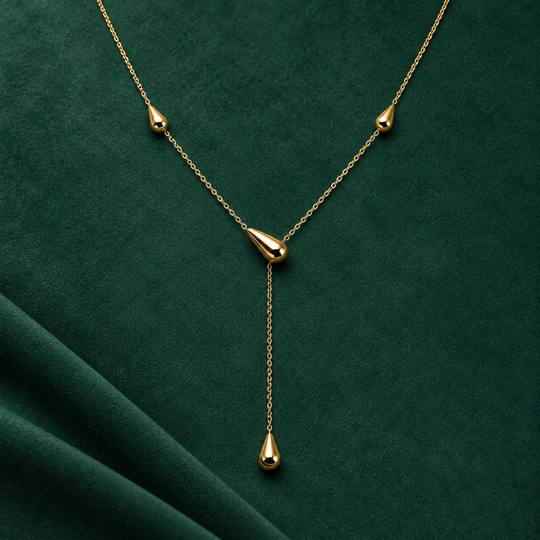 Gold-tone 316L stainless steel necklace with a fine cable chain, teardrop charms and a long drop pendant, laid flat on green velvet