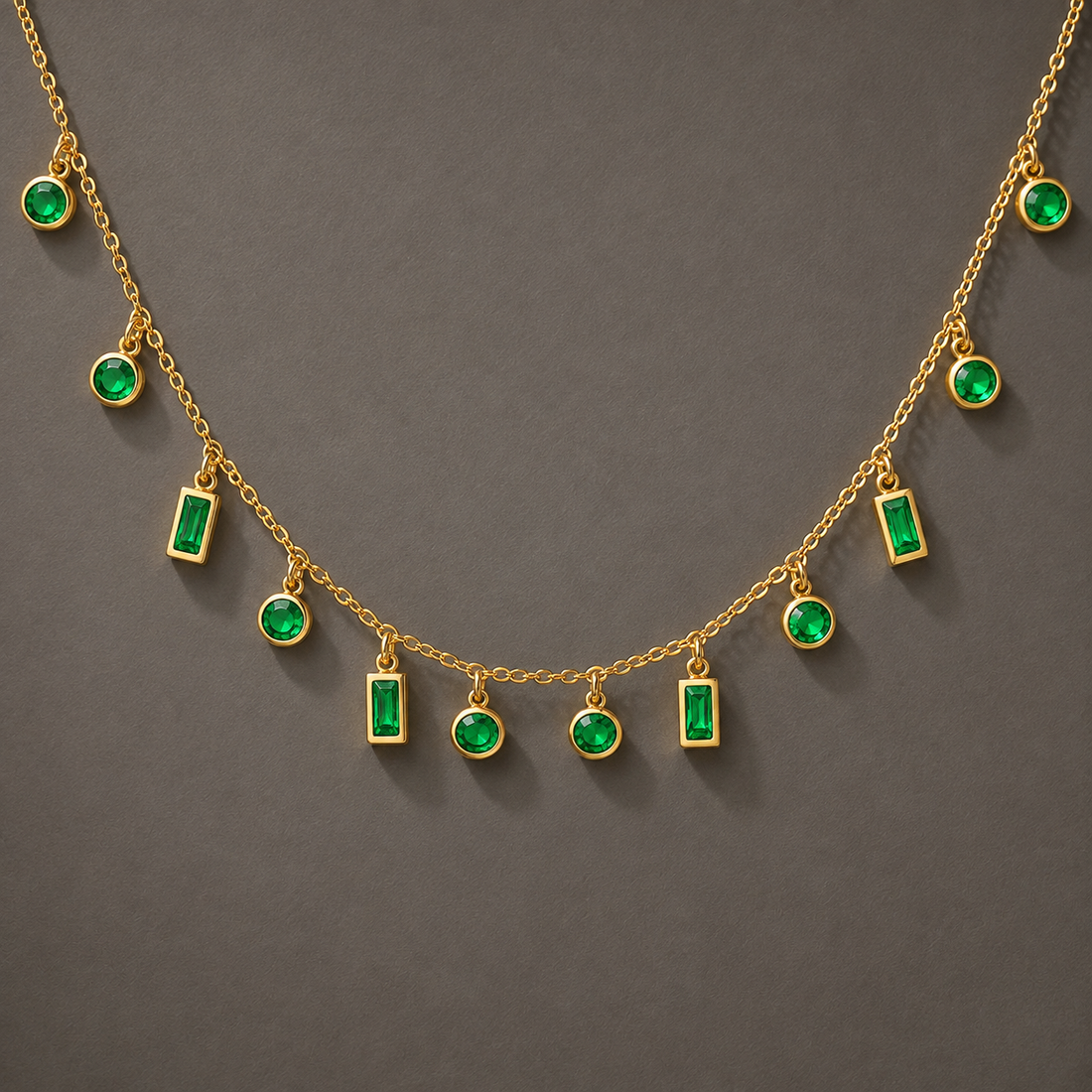 Gold chain necklace with multiple dangling emerald-cut green gemstone charms and round green gemstone accents, displayed against a dark gray background.