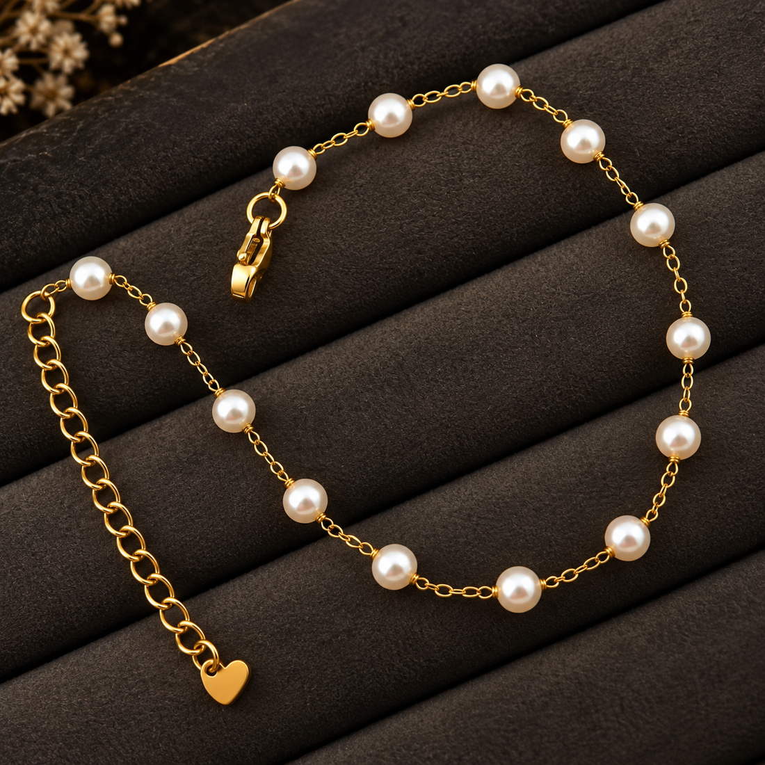 Gold-tone 316L stainless steel anklet with white pearl beads spaced along a fine chain and a heart charm on the extender, laid flat on a dark display
