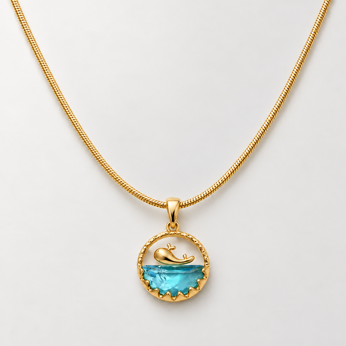 Gold-tone 316L stainless steel pendant necklace with a gold whale motif above a blue faceted stone in a scalloped round frame, on a snake chain