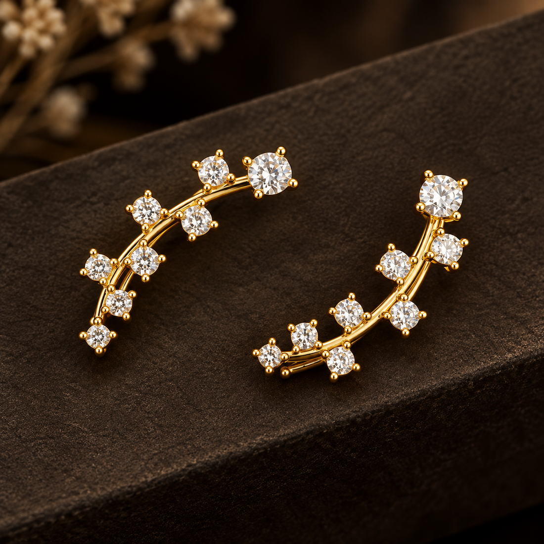 Gold-tone brass climber earrings with a curved bar set with clear round stones, a pair shown on a dark surface