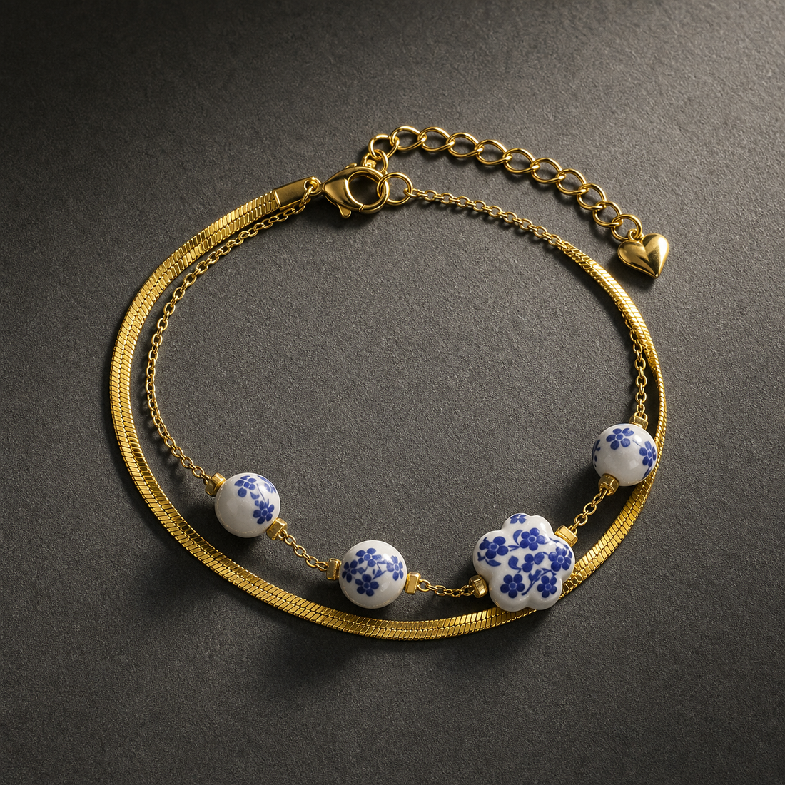 One wrist-worn chain bracelet in yellow-gold-tone metal with a polished finish. It has two connected strands sharing one clasp assembly: a wide, flat, flexible snake/herringbone-style band of fine gauge, and a much thinner fine-link cable chain that carries all the beads.
