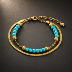 One wrist-worn chain bracelet in yellow-gold-toned metal with a polished finish. It has two parallel strands joined at common end terminals: one strand is a flat, flexible herringbone (snake) chain of fine gauge with no attached components; the other is a fine cable-link chain strung with beads.
