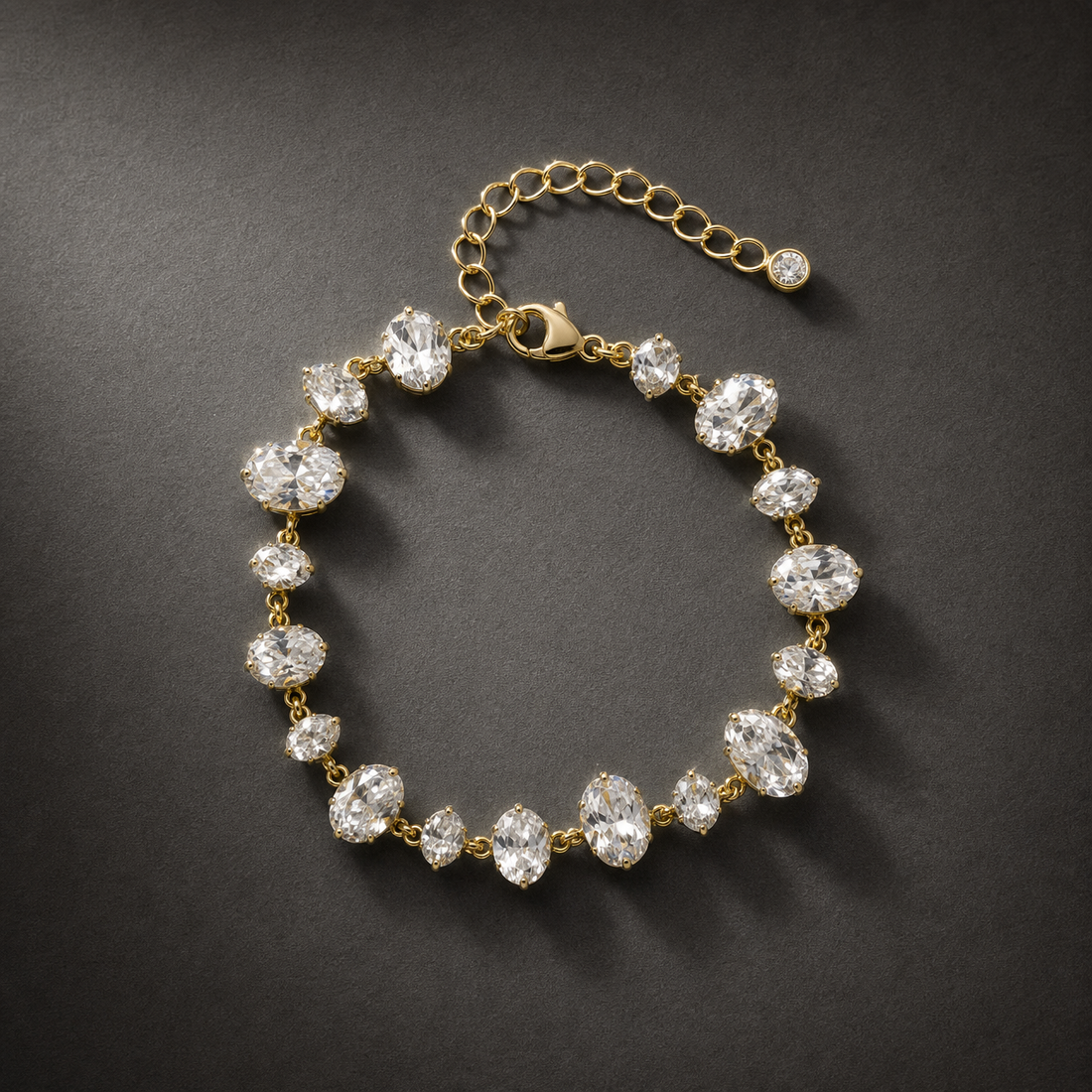 One wrist-worn chain bracelet. Gold-toned metal with polished finish; single flexible strand. Construction is a stone station chain: clear faceted elements in gold-tone prong cups, joined by small metal rings, plus a finer oval/curb-link extender. The main stone-bearing run is approximately 18–20 times the width of the largest oval station; the extender is about one-quarter of the main chain length. A working lobster-type clasp is visible.