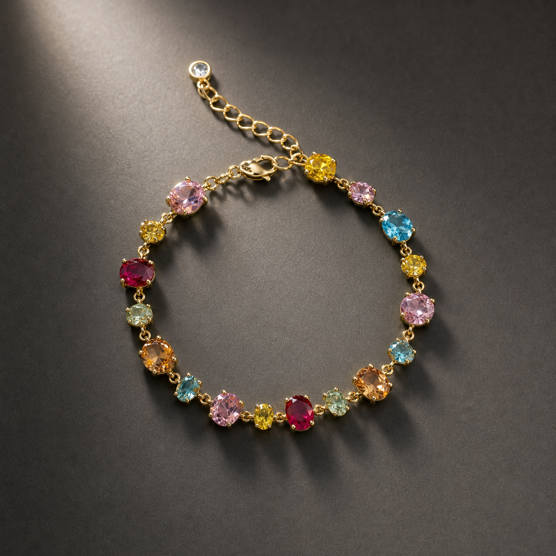 One wrist-worn chain bracelet in yellow-gold-toned metal with a polished finish. Single strand: a fine-gauge link chain carrying a continuous run of individually set, claw/prong-mounted faceted oval and round stones in mixed colours, linked directly stone-to-stone with tiny connector links; the largest ovals are the dominant components. The chain run is roughly 22–25 times the width of the largest oval stone; the extender is about one-third of the main chain length.