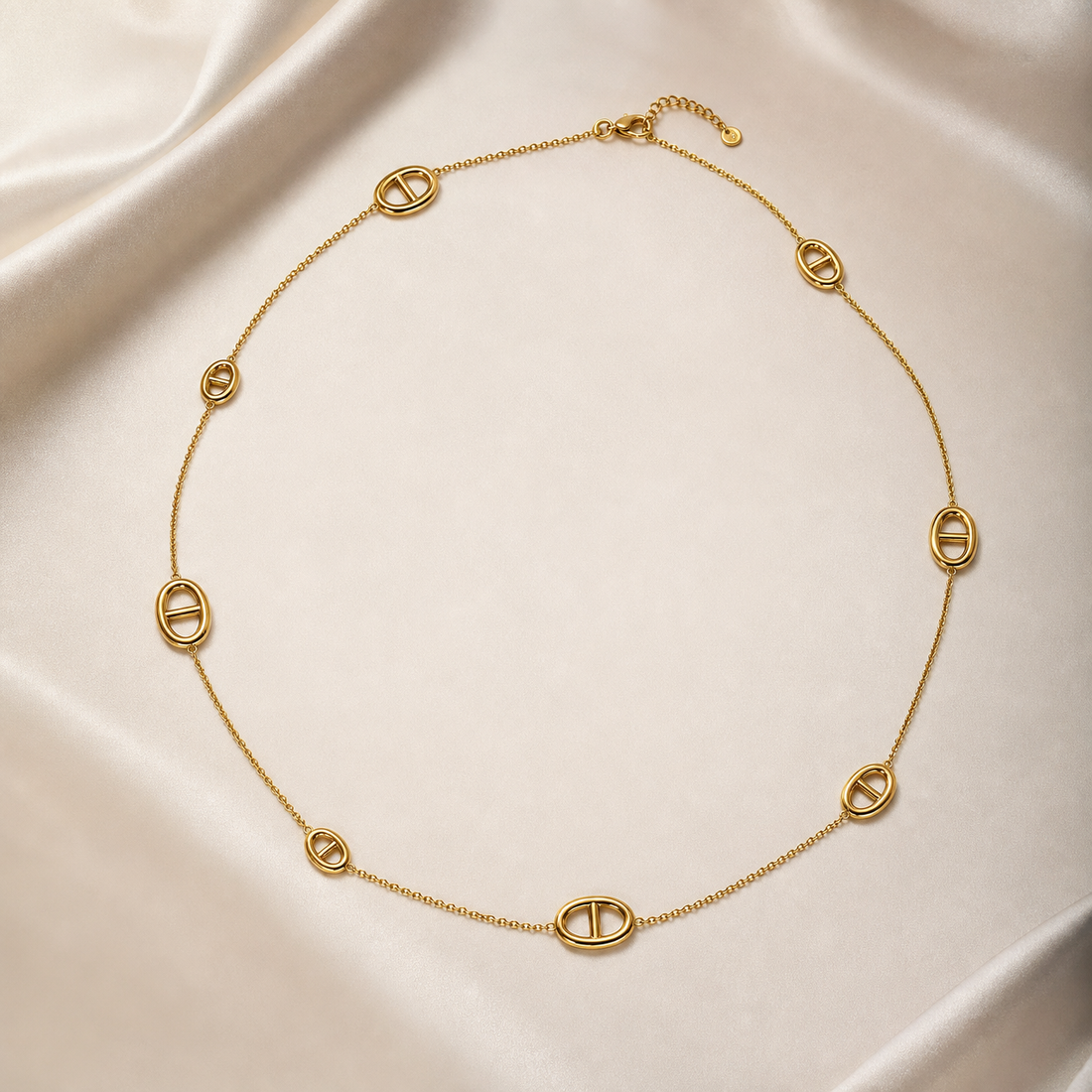 One single-strand station necklace in yellow-gold-toned metal with a polished finish, laid open in a rough square. The chain is a fine, small-gauge round-link cable chain carrying 8 fixed oval solid-metal stations at irregular spacings; each station is an open oval ring with a single straight bar spanning its centre, the bar integral to the oval rather than set or mounted, and there are no stones, beads or charms.