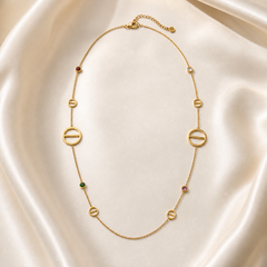 A single gold-tone necklace with a polished yellow-gold finish, built as one long fine cable chain of small gauge, worn doubled into two roughly parallel hanging runs joined at the top by a lobster clasp with a short extender chain of 5 links terminating in 1 small round ball tag. Along its length sit 10 flat, solid-metal open-ring motifs, each a circle bisected by a horizontal bar, fixed inline with the chain; 2 are larger diameter, 8 are smaller, distributed asymmetrically with varying spacing.