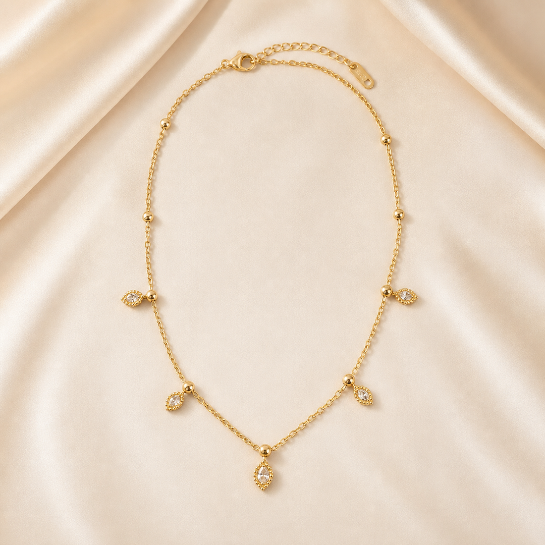 A single gold-toned necklace with a polished yellow-gold finish, built from one fine cable-link chain of small oval links forming a single continuous strand. From the clasp end the chain runs past a series of small polished spherical beads threaded as fixed stations, spaced irregularly: the first two beads occur on plain chain sections, then further beads appear at the points where charms hang.