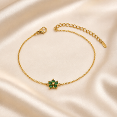 A single flexible bracelet in yellow-gold-toned polished metal, built from one strand of fine oval cable-link chain of light gauge. From the lobster-clasp end, a plain run of chain leads to the single decorative station: a small flower motif set with five round faceted green stones arranged as petals in individual prong/claw settings around a small solid gold-toned domed centre, with tiny gold bead accents between some petals; the flower is fixed inline to the chain via small connector loops and lies flat