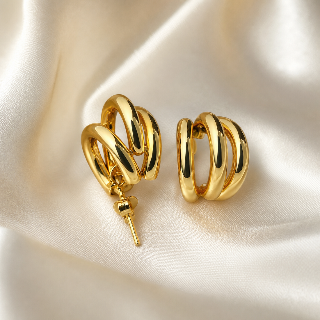 A matched pair of two hoop earrings in yellow-gold-coloured metal with a high-polish, mirror-like finish. Each earring is constructed from two interlocked or concentric smooth rounded tube hoops of slightly different diameters, one nested within the other so they cross and overlap, creating a layered double-hoop silhouette with a domed, channelled relief where the bands cross; the hoops are of medium, even gauge with no stones, pendants, charms or engraving.