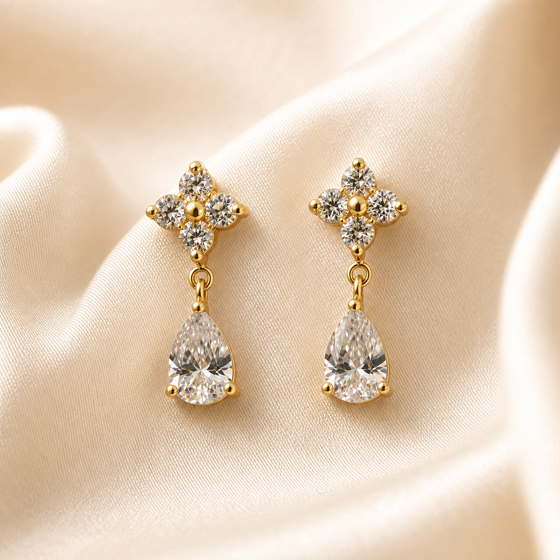 A matched pair of drop earrings, two items total, in a warm gold-coloured polished metal. Each earring comprises a stud top formed as a cross or four-lobed motif and a dangling drop below it. Each stud carries four small round clear faceted stones set as the four arms of the cross, held in small prong or claw settings with gold-coloured bead tips at the outer points, and a single small solid gold-coloured round bead at the centre of the cross.