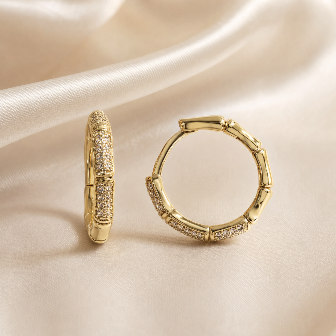 A matched pair of small hoop earrings, two items total, in polished yellow gold-tone metal with a high-shine finish. Each hoop is a continuous ring of medium gauge built as a repeating bamboo-style segmented motif: rounded tubular metal links alternating with sections set with a continuous field of tiny colourless clear stones in pavé-style setting, the individual stones too small to count reliably.