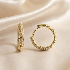 A matched pair of small hoop earrings, two items total, in polished yellow gold-tone metal with a high-shine finish. Each hoop is a continuous ring of medium gauge built as a repeating bamboo-style segmented motif: rounded tubular metal links alternating with sections set with a continuous field of tiny colourless clear stones in pavé-style setting, the individual stones too small to count reliably.