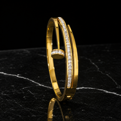 A single rigid bangle in polished yellow gold, high-shine finish. The band is a flat cross-section strip roughly one-twentieth of the outer diameter in width, even all the way round with no swelling. It is an open cuff: the band ends overlap and cross past each other, leaving a gap approximately equal to the band width, with one end terminating in a round flat disc end cap edged with small round colourless stones in a pavé-style setting.