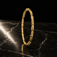 A single rigid gold-toned bangle with a high-polish finish. The band is slender, roughly one-twentieth of its outer diameter in width, with a rounded cross-section, and swells at intervals into elongated smooth barrel-shaped segments, each about twice the band width, separated by clusters of small stacked round spacer beads; this alternating barrel-and-bead pattern repeats evenly around the whole circumference.