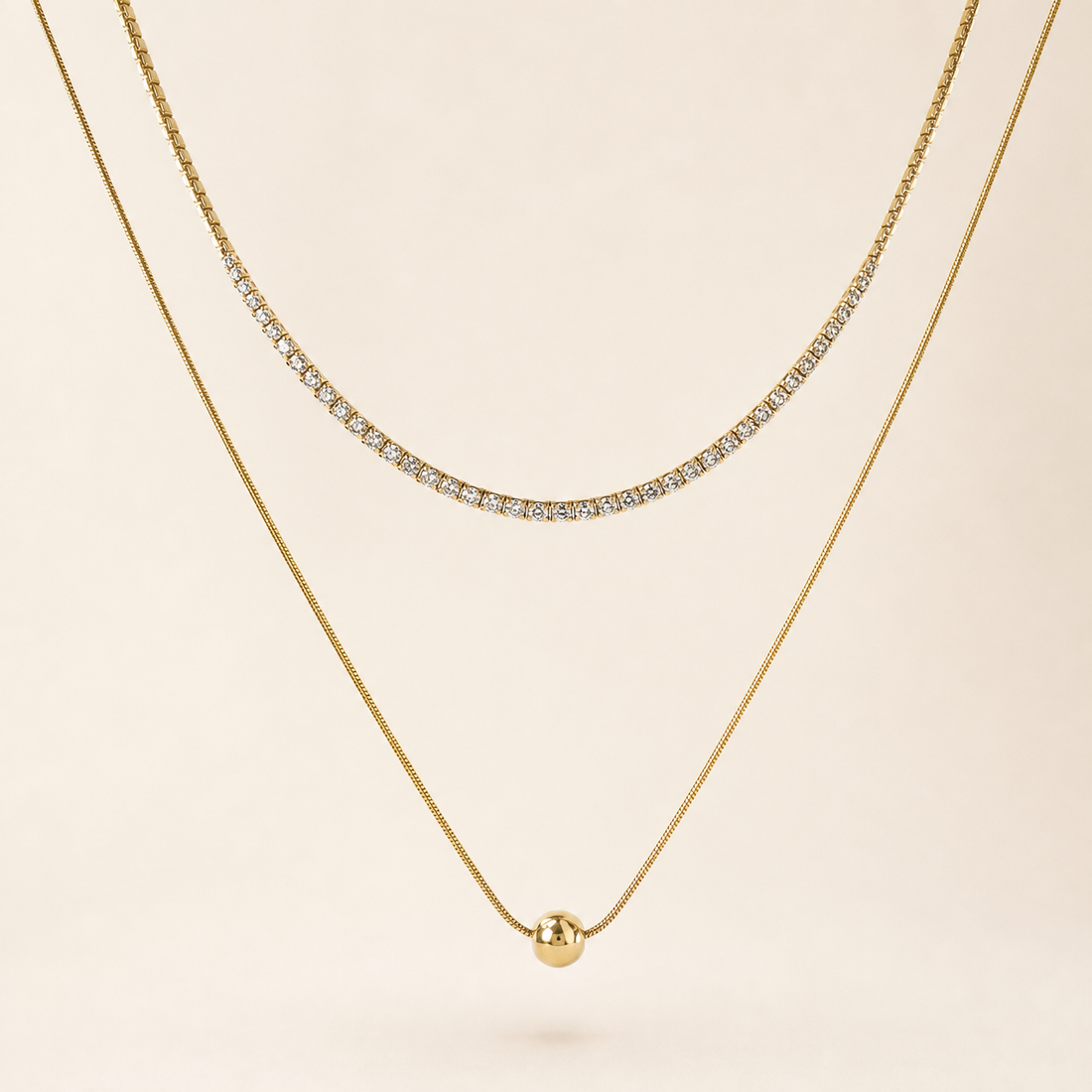 Two separate gold-tone necklaces, polished finish. Necklace one is a single-strand tennis-style chain of small clear round faceted stones, each in an individual gold box/prong mounting linked in a continuous articulated line; stone count is not clearly resolvable at the clasp ends and is withheld, stones are uniform and tightly spaced with no gaps; chain run is roughly 60-70 times one stone width, no extender visible.