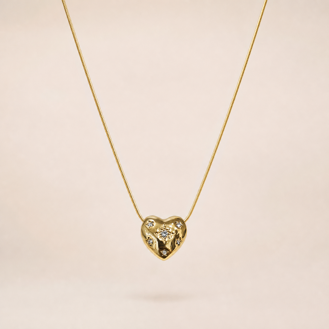 Single pendant necklace. Yellow-gold-tone metal with a polished finish. Construction is one fine round snake chain of small gauge, a single continuous strand with no branches, passing directly through a fixed heart-shaped pendant so the pendant sits centrally on the chain run. The visible chain run is approximately thirty times the width of the heart pendant; no extender chain is visible, and no working clasp is visible in the image, so closure, extender and terminal-tag details cannot be confirmed.