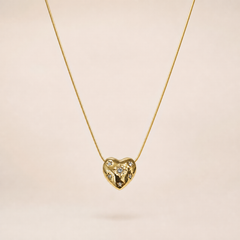 Single pendant necklace. Yellow-gold-tone metal with a polished finish. Construction is one fine round snake chain of small gauge, a single continuous strand with no branches, passing directly through a fixed heart-shaped pendant so the pendant sits centrally on the chain run. The visible chain run is approximately thirty times the width of the heart pendant; no extender chain is visible, and no working clasp is visible in the image, so closure, extender and terminal-tag details cannot be confirmed.