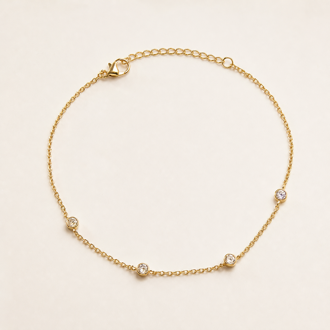 One anklet: a yellow-gold-tone, bright-polished flexible ankle chain made as a single fine cable-link strand of small oval links. The main chain run is approximately eighty times the width of the largest station; the adjustable extender is about one quarter of the main-chain length. A working lobster-claw clasp is visible.