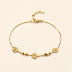 One anklet in yellow-gold-toned metal with a bright polished finish. It is a single-strand fine box chain of small, uniform square links, forming a closed flexible loop with no branches. The chain run measures roughly 25 times the width of the largest component (a flower charm); the curb-link extender chain is about one-fifth the length of the main chain. A working lobster clasp is visible at the junction.