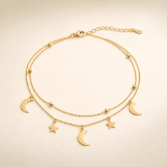 One anklet in yellow-gold-toned metal with a polished finish. It is built as two parallel fine cable-chain strands of small-gauge oval links joined at a single lobster clasp, giving a double-strand topology along most of the chain run. The full chain run is approximately 16 to 18 times the width of the largest crescent-moon charm, and the short extender chain near the clasp is roughly one-tenth of the main chain length.