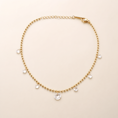 One anklet only: a single flexible yellow-gold-tone polished chain in a fine small-ball/bead construction, with one short oval-cable-link extender section and one visible working lobster-claw closure; no terminal tag is clearly resolved. The main chain run is approximately 30 times the width of the largest dangling component, and the extender is roughly one-eighth of the main chain length.