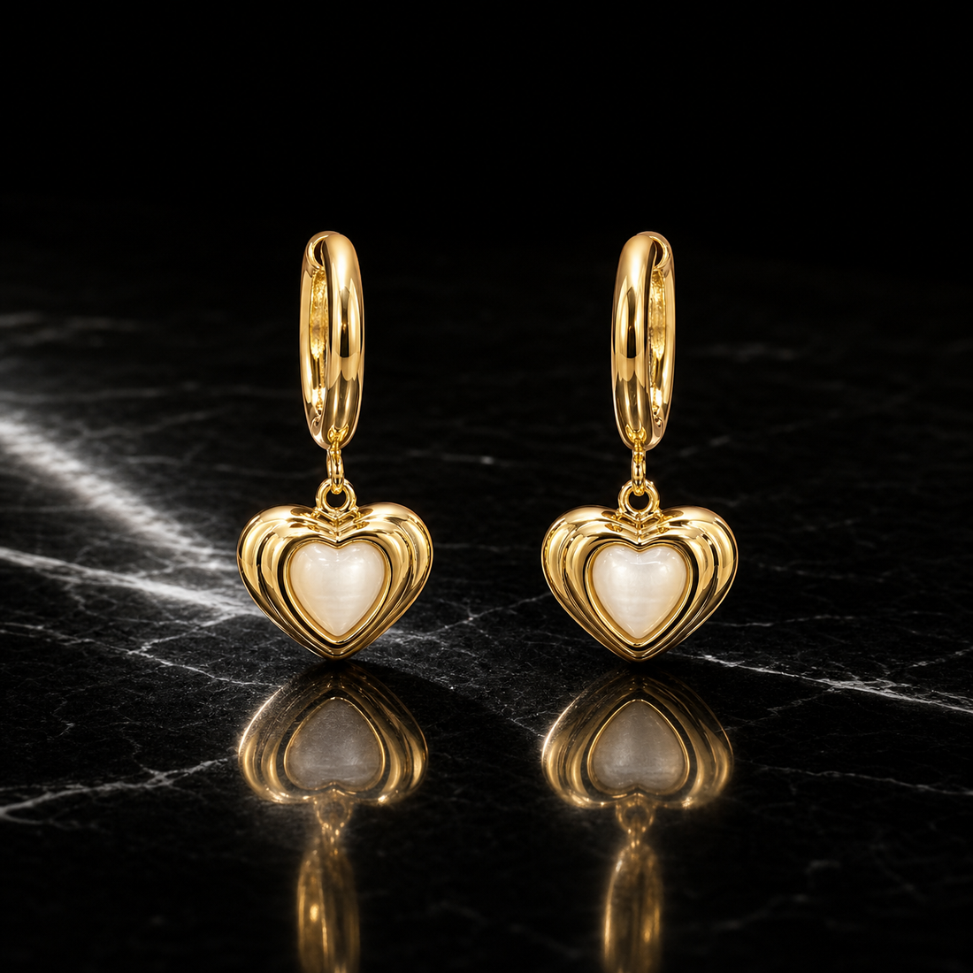 Two earrings, one pair, in polished gold-toned metal with a reflective finish. Each has a small huggie-hinge hoop fitting of short length and standard gauge; the total drop is approximately twice the widest part. Three articulated sections hang from one another: the hoop, a small connector link that hinges freely, and a heart dangle.