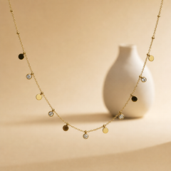 One gold-tone station necklace of a single fine cable chain with polished finish, carrying alternating dangling charms and small round bead stations spaced along the chain. The chain run is roughly 30 times the width of the largest disc component; no extender is visible, and the chain ends leave the frame, so the closure is not visible and clasp and extender type cannot be confirmed.