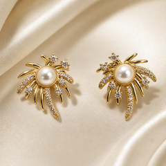 A matched pair of stud-style earrings, two items total, in yellow-gold-tone metal with a high-polish finish. Each earring is a single solid-cast sunburst or firework motif: a domed white round pearl-like bead sits in a smooth bezel cup at the centre, surrounded by radiating solid-metal rays of varying length, some rays smooth and plain, others pave-set with small clear faceted round stones.