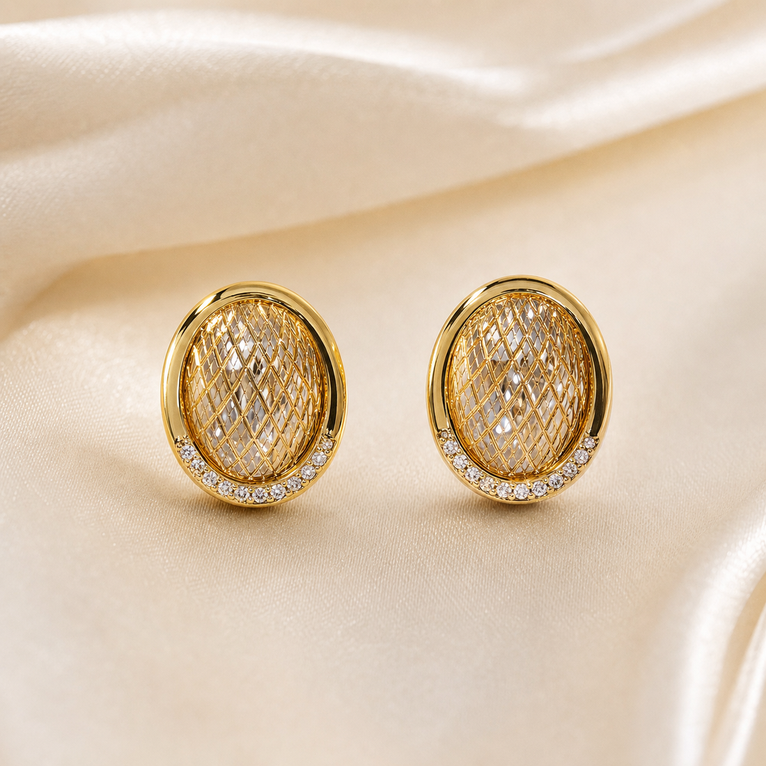 A matched pair of two stud earrings in yellow-gold-coloured metal with a polished finish. Each earring is a solid, oval, slightly domed plaque: the face carries a raised criss-cross lattice of polished diagonal ribs forming a diamond-quilted relief over a reflective ground.
