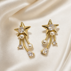 A matched pair of two drop earrings in polished yellow-gold-tone metal. Each earring has a stud-style top formed as a solid five-pointed star with domed, polished relief, its centre holding one large round brilliant-cut clear faceted stone in a prong setting. Beneath the star, one small white round faux pearl is fixed at the junction where three curved, slender gold-tone bar strands hang freely; the strands are of slightly differing lengths and each terminates in a dangling element.
