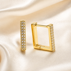 A matched pair of two small square-shaped huggie hoop earrings in yellow-gold-tone metal with a polished finish. Each earring is a rigid rectangular hoop with rounded corners and a hinged closure, the post and hinge visible at the top edge of one earring; the band is of medium gauge with flat side walls and a smooth inner face.