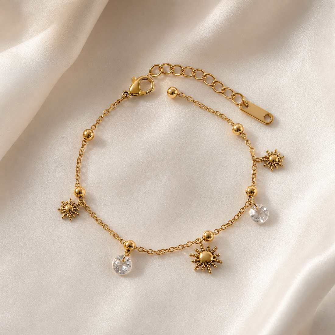 One wrist-worn chain bracelet in polished yellow-gold-tone metal. It is a single continuous strand of fine cable chain interspersed with small polished spherical gold bead stations, with a working lobster clasp at one end and, at the other, an extender of larger round links terminating in a flat oval metal tag. The main chain run is roughly eighteen to twenty times the width of the largest charm, and the extender is about one quarter of the main chain length.