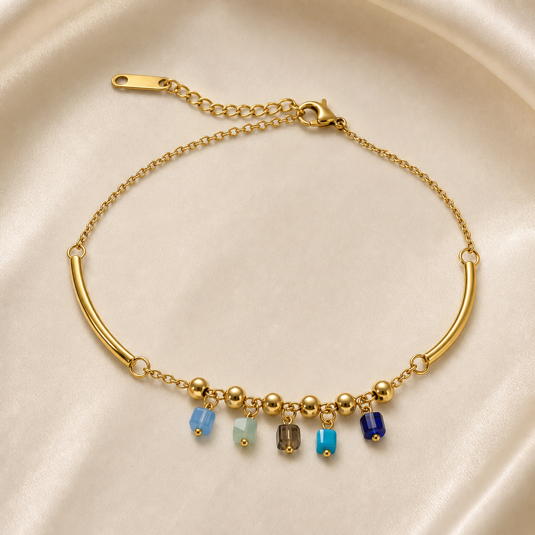 One anklet, gold-tone metal with a polished finish. It is a single fine-gauge cable chain whose run is interrupted by two long curved hollow tube segments joined to the chain by jump rings. Total chain run is roughly 25 times the width of the largest component (the tube bars), and the curb-link extender is about one quarter of the main chain length. A working lobster clasp is visible, connecting to the extender chain, which ends in one flat elongated terminal tag.