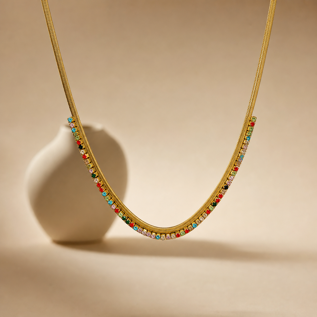 One necklace. Gold-coloured metal with a polished finish, formed as a single flat, flexible woven chain of herringbone/snake type with a fine, tight gauge; no branches, joins or second strand. The visible chain run is roughly 60 to 70 times the width of one stone setting. No extender is visible, so no extender fraction can be stated; the closure is partly obscured and no working clasp, extender chain or terminal tag is resolvable.