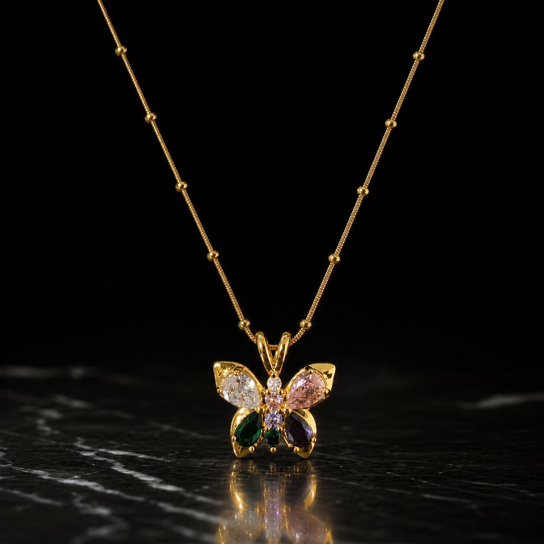 One gold-tone pendant necklace with a polished finish. It is a single fine snake chain studded with small round metal beads at intervals, of fine gauge, carrying one butterfly pendant suspended from a split double-loop bail. The visible chain run is roughly fifteen to twenty times the pendant's width; no clasp, extender or terminal tag is visible, as both chain ends run out of view, so the closure state is unconfirmed and the piece is partly obscured.