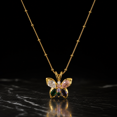 One gold-tone pendant necklace with a polished finish. It is a single fine snake chain studded with small round metal beads at intervals, of fine gauge, carrying one butterfly pendant suspended from a split double-loop bail. The visible chain run is roughly fifteen to twenty times the pendant's width; no clasp, extender or terminal tag is visible, as both chain ends run out of view, so the closure state is unconfirmed and the piece is partly obscured.