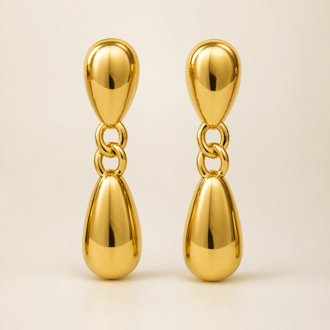 Two ear-worn earrings of one design in yellow-gold-tone metal with a high-polish mirror finish. Each is a drop earring on a post fitting (the posts and backs are partly obscured) emerging from a domed, hollow teardrop stud. From the stud hangs a short articulated chain of two interlocking oval links, ending in a larger solid-metal teardrop dangle, so each earring has three sections hinging at two joints. The total drop is roughly three times the widest teardrop width.