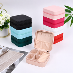 Blush pink zip-closed jewellery travel case open to show compartments, ring slots and earring holder, with stacked cases in other colours behind