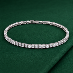 Silver-tone brass tennis bracelet with square-cut clear stones in a line setting and a box clasp, shown lying flat on a green cloth, second view