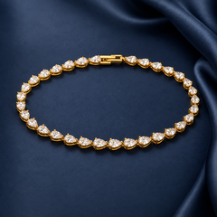 Gold-tone brass tennis bracelet with pear-cut clear stones in prong settings and a box clasp, laid flat on dark blue fabric