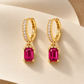 Gold-tone 316L stainless steel huggie hoop earrings with a crystal-set front and a rectangular pink-red stone drop, shown as a pair