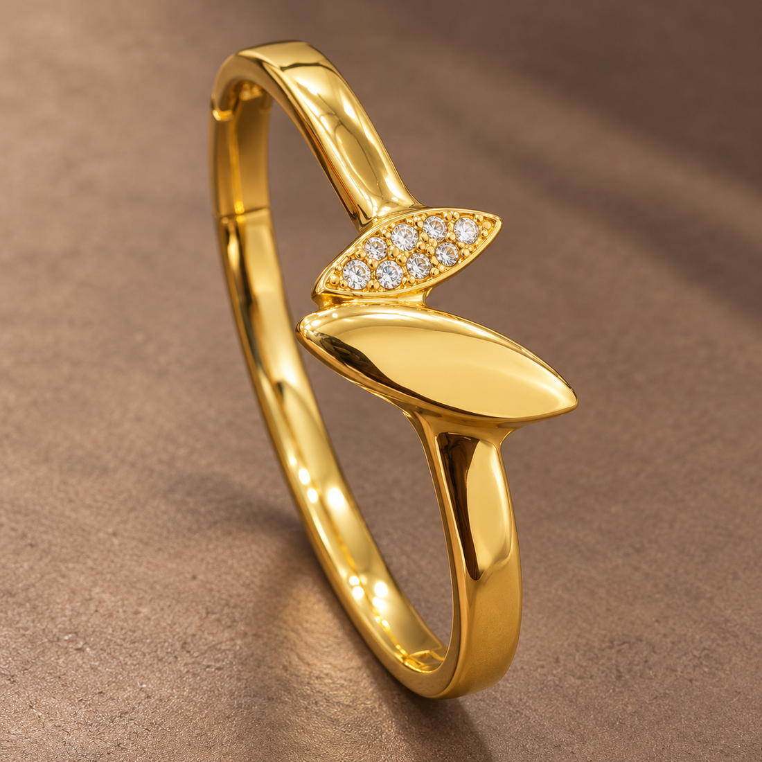 Gold-tone 304 stainless steel kada bracelet with a polished leaf motif and a row of clear stones on the upper leaf, shown from an angle