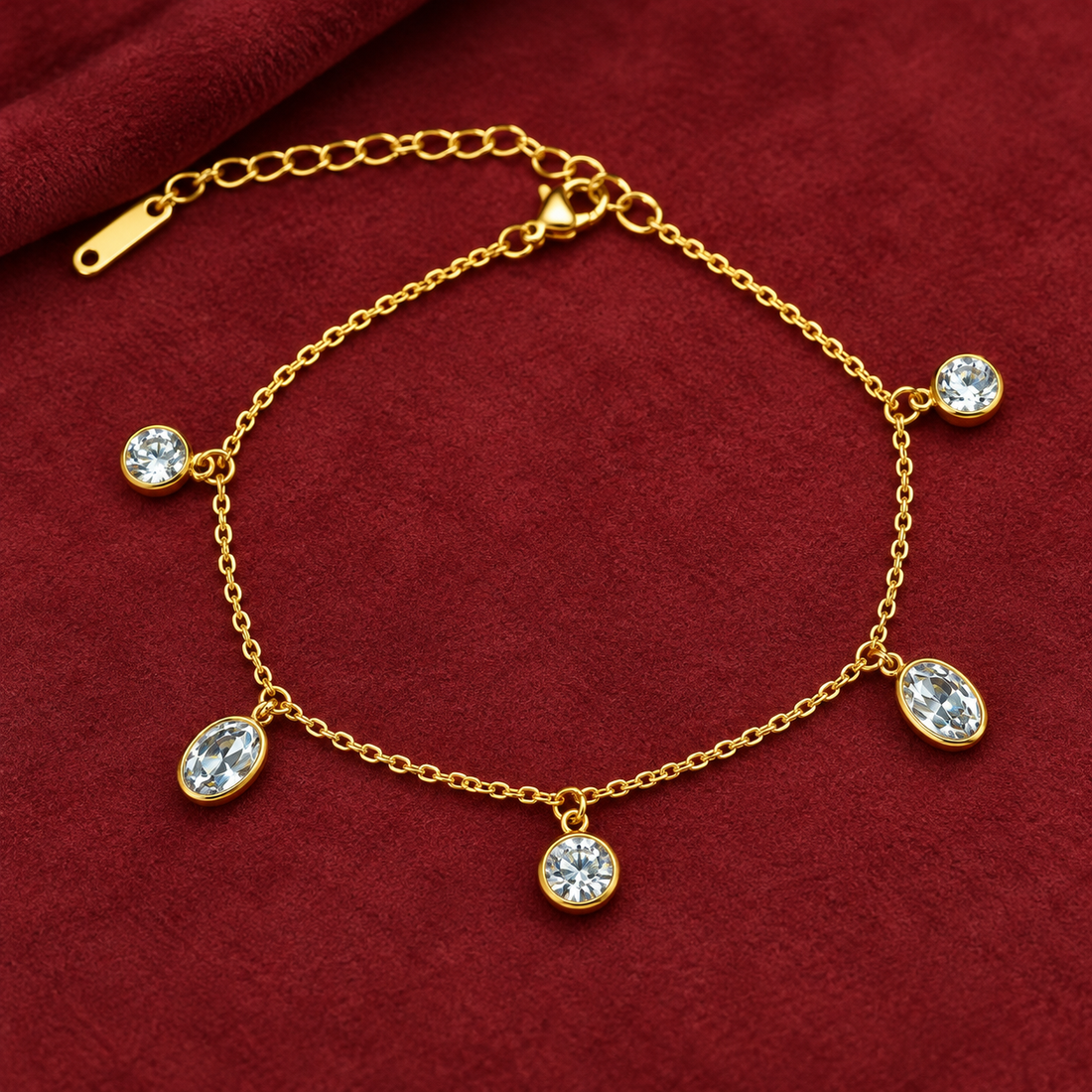 Gold-tone 304 stainless steel chain bracelet with five bezel-set clear crystal drops hanging from a fine cable chain, lying flat on red fabric