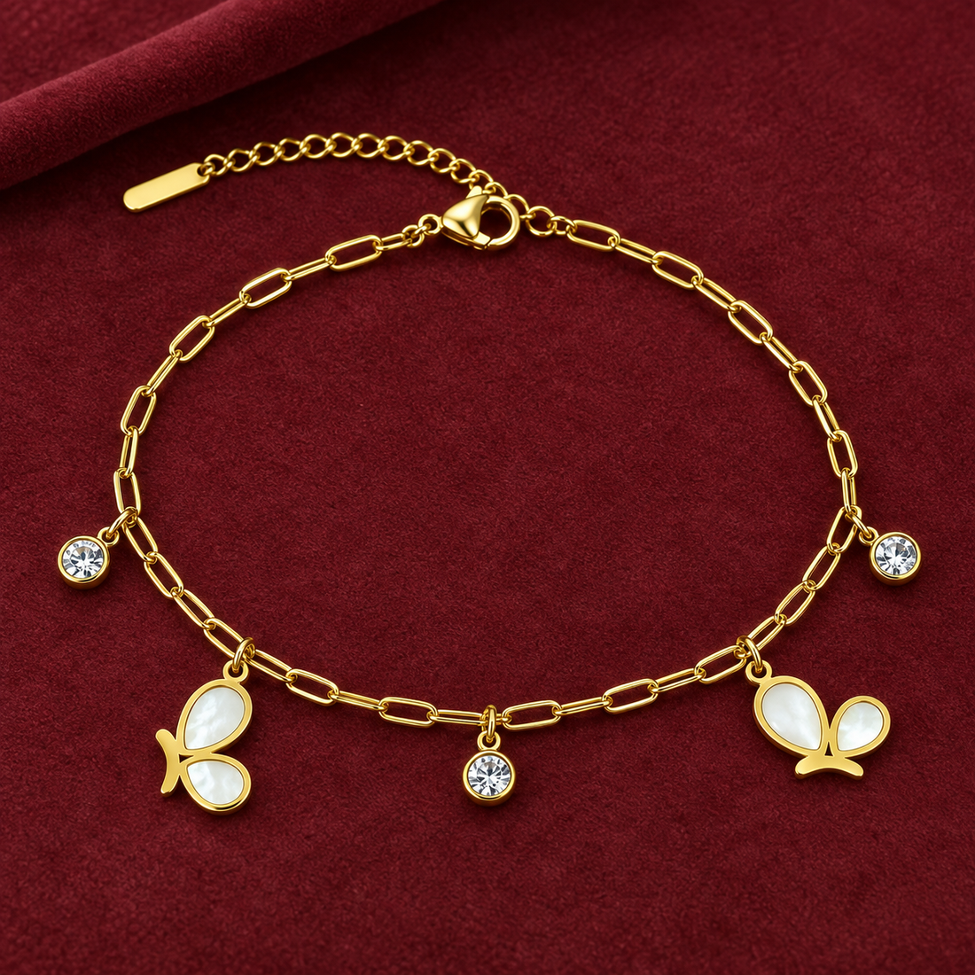 Gold-tone 304 stainless steel anklet with an oval link chain, two white shell butterfly charms and three crystal-set drops, laid flat on red velvet