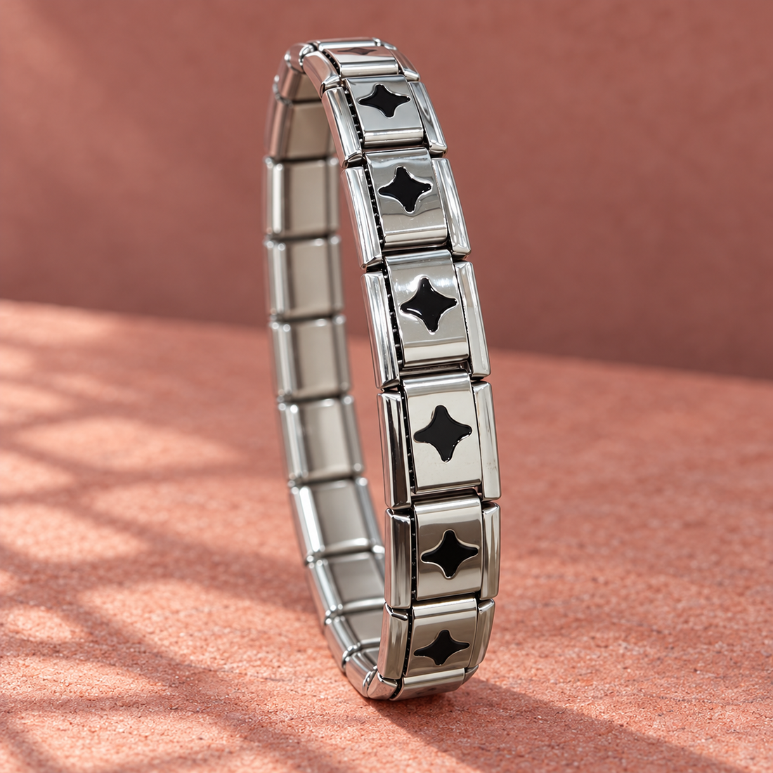 Silver-tone 304 stainless steel stretch bracelet with rectangular links and black four-point star enamel inserts, shown standing on a surface