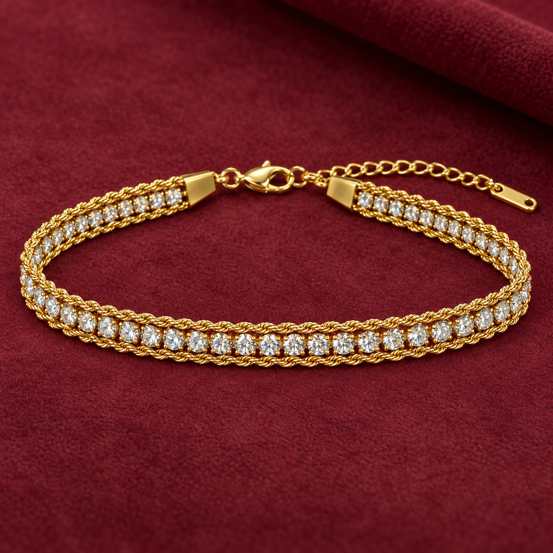 Gold-tone 316L stainless steel bracelet with a rope-twist band and a row of clear crystals in claw settings, laid flat on a maroon cloth