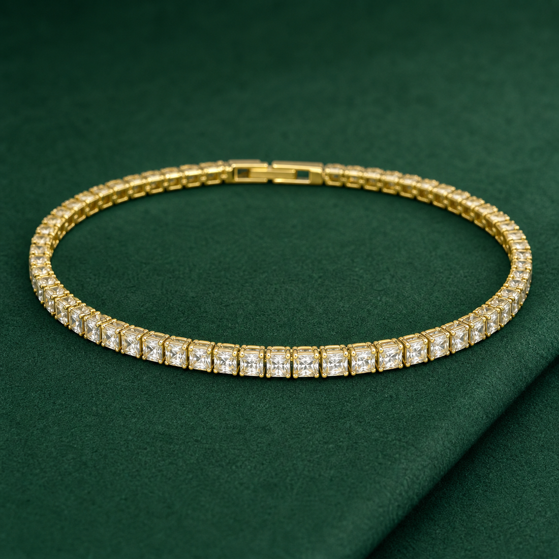 Gold-tone brass tennis bracelet with square clear stones in claw settings and a box clasp, laid flat on a green surface